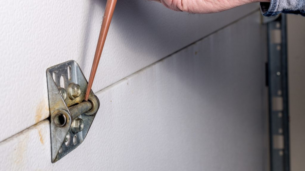 A user applying lubricant on hinges to prevent premature garage door hinge replacement