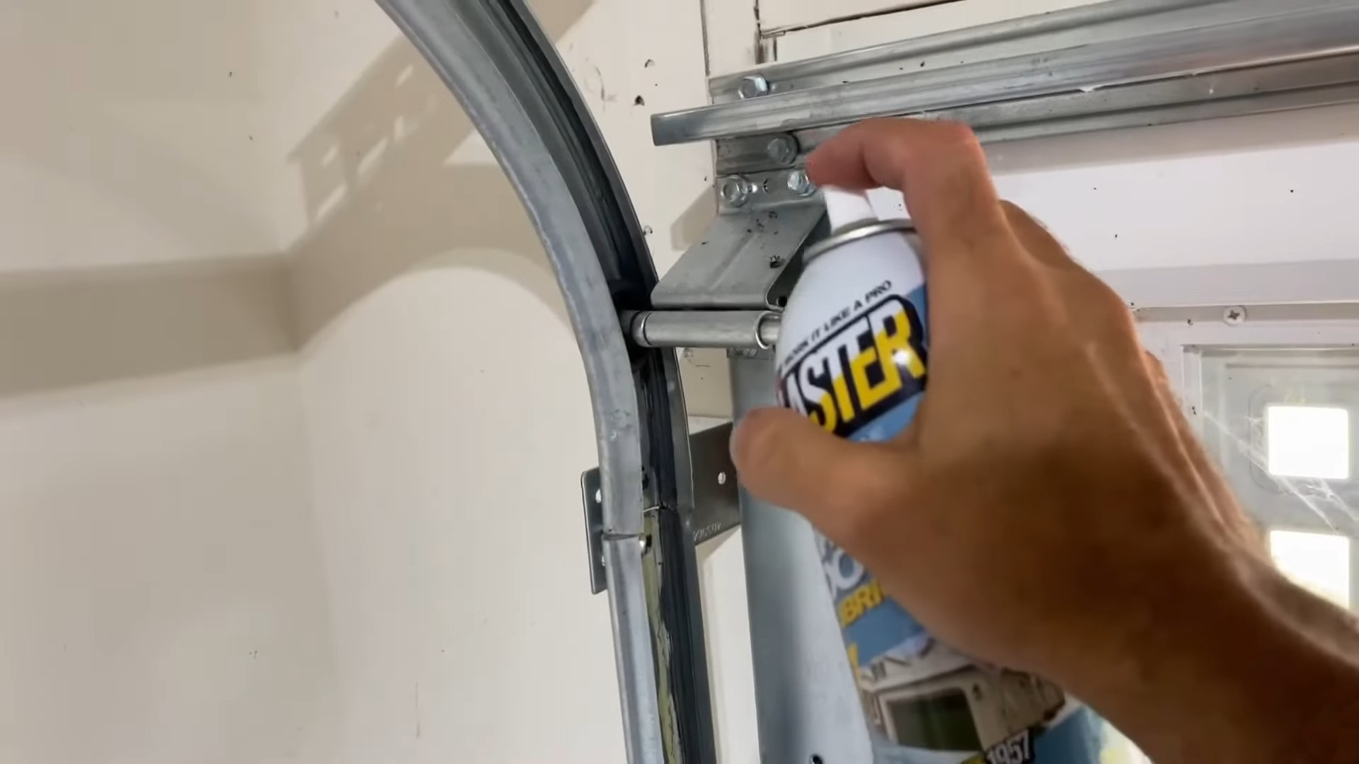 Applying silicone spray lubricant to garage door rollers and tracks for smoother operation