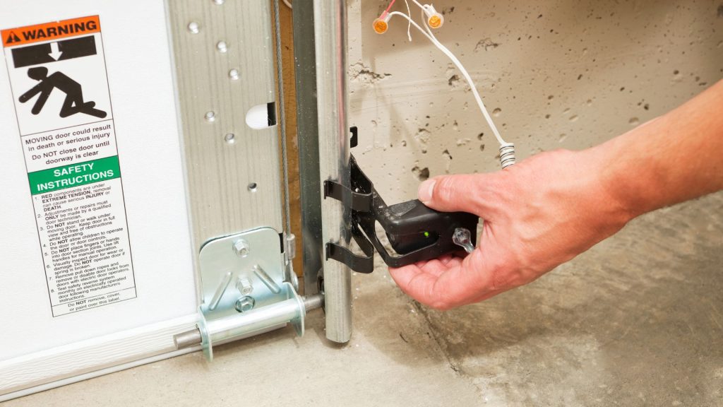A man realigning the garage door safety sensors